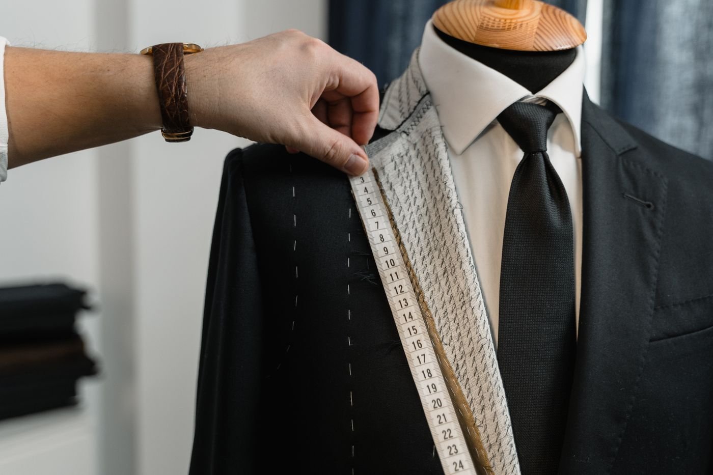 Representative photo of a tailor holding a tape measure to a black suit jacket on a dress form