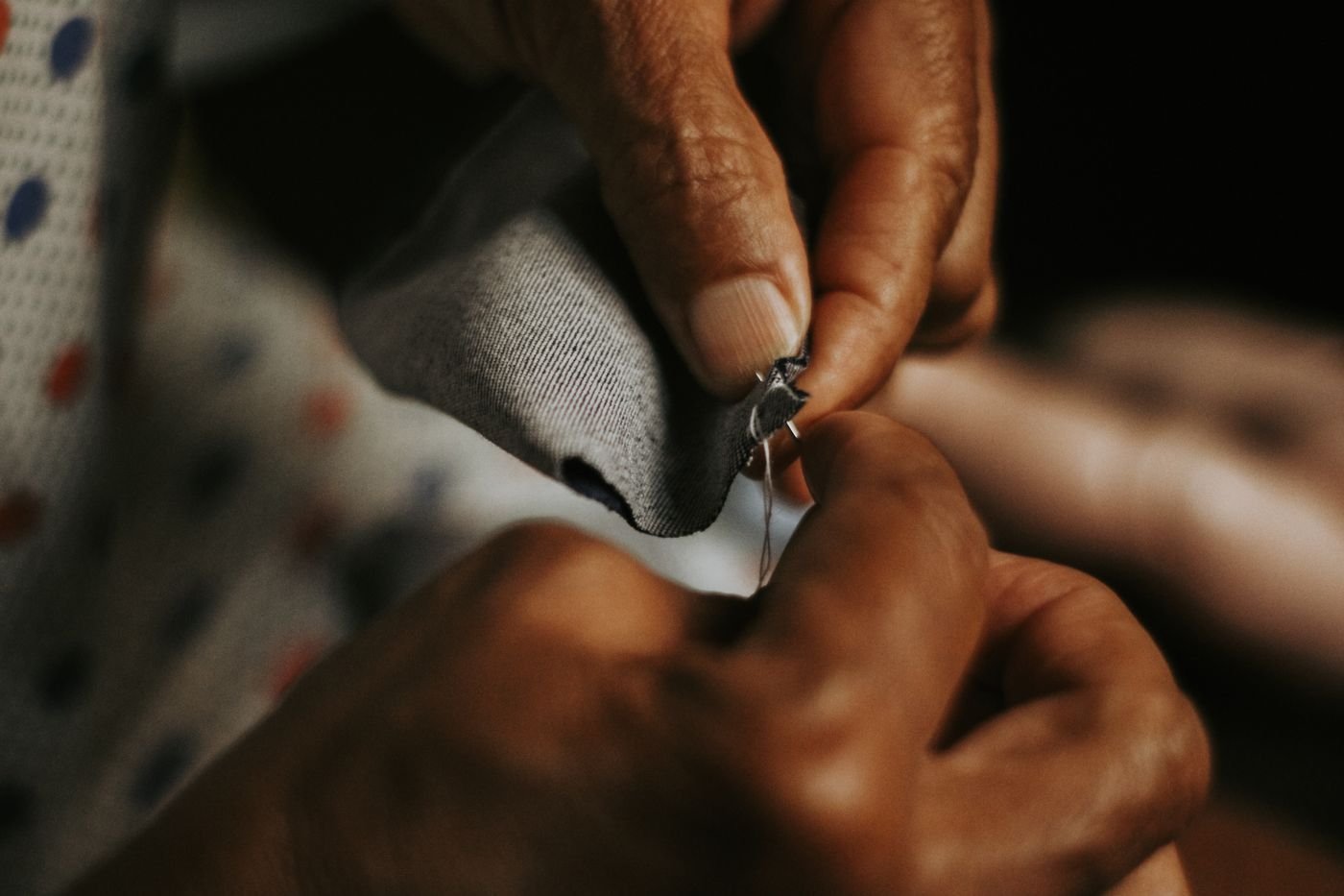 Representative photo of a tailor hand-stitching a hem on a garment with needle and thread