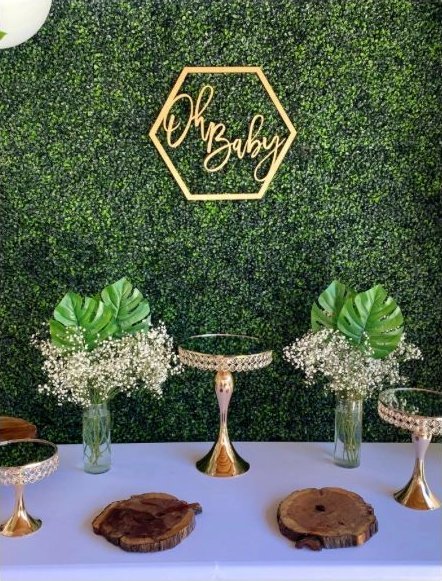Representative photo of a boxwood hedge wall with a gold Oh Baby hexagon sign and gold dessert stands with baby's breath