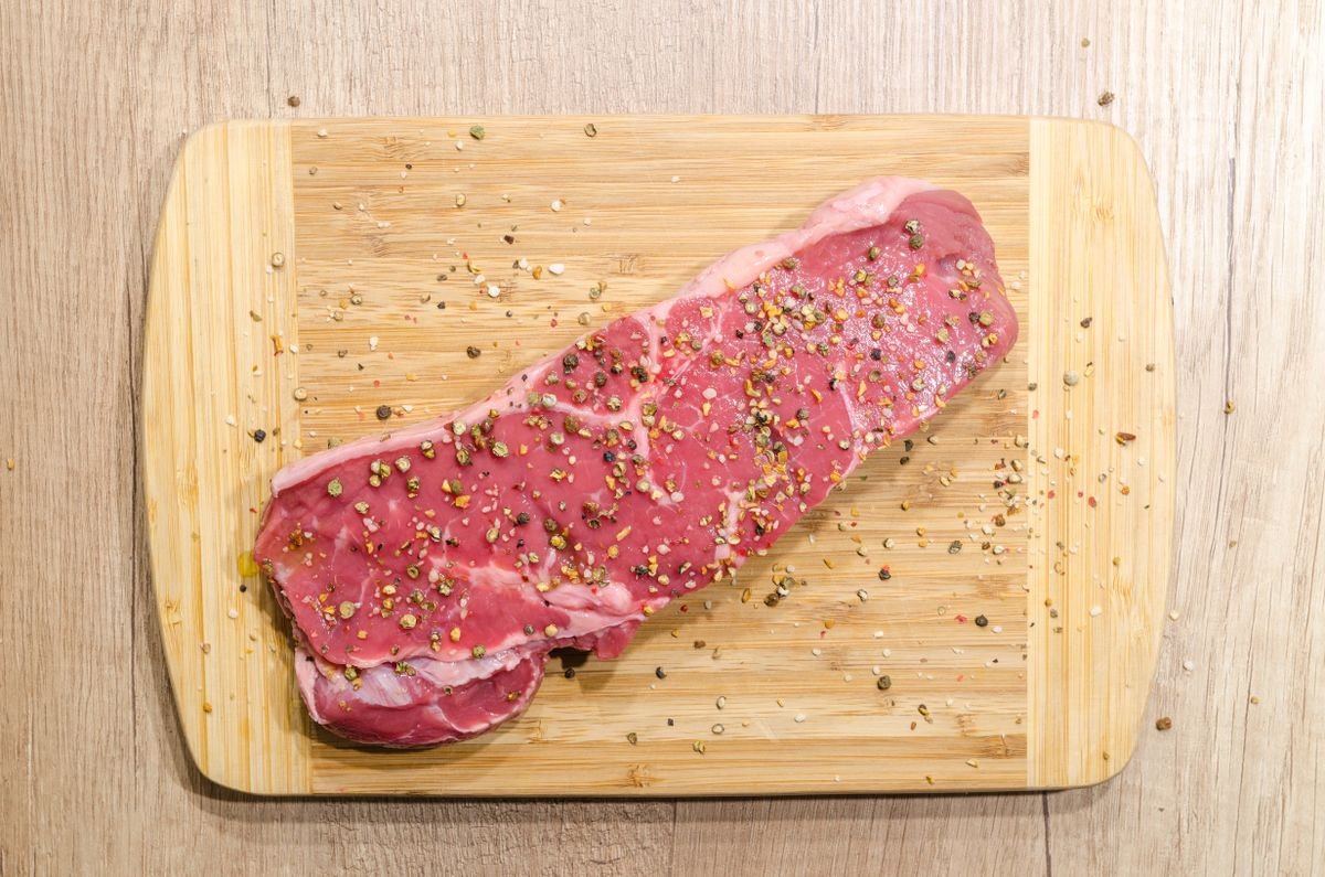 Representative photo: fresh-cut, seasoned strip steak on a cutting board.