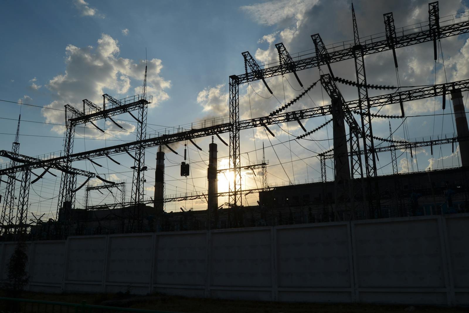High-voltage substation silhouetted against a dramatic sunrise — switchgear, busbars, and steel structures backlit by the morning sun.