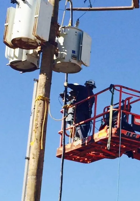 Electrical crew working near substation transformer equipment from an aerial lift.