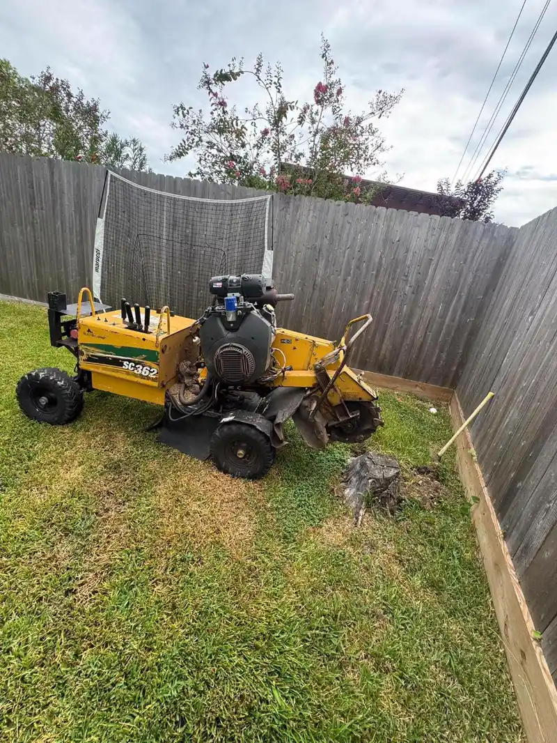 Grinder maneuvered into a narrow side yard between a wood fence and a batting cage
