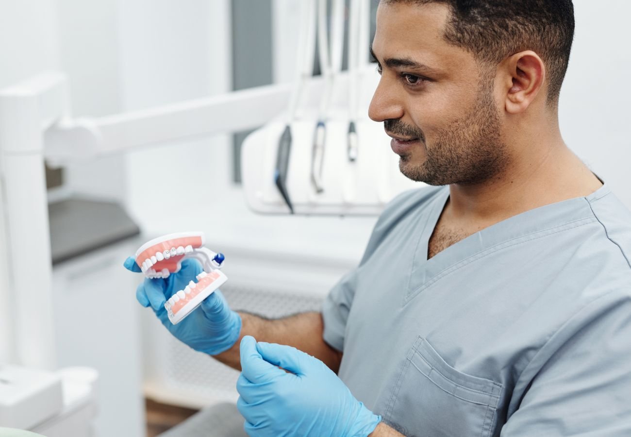 Representative photo of a dentist in scrubs holding a dental model while explaining care to a patient